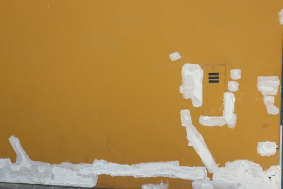 A textured yellow wall with patches of white paint.